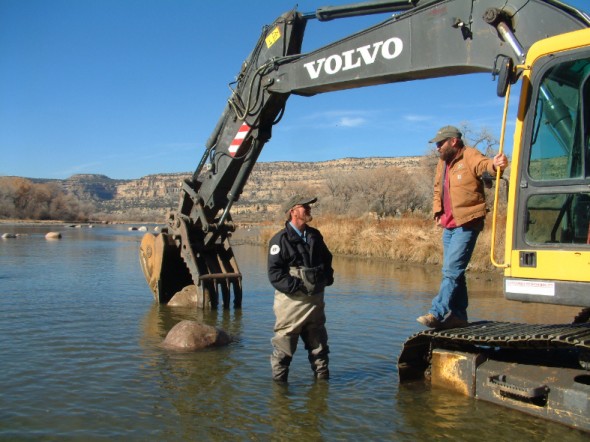 men talking by heavy equipment in san juan river